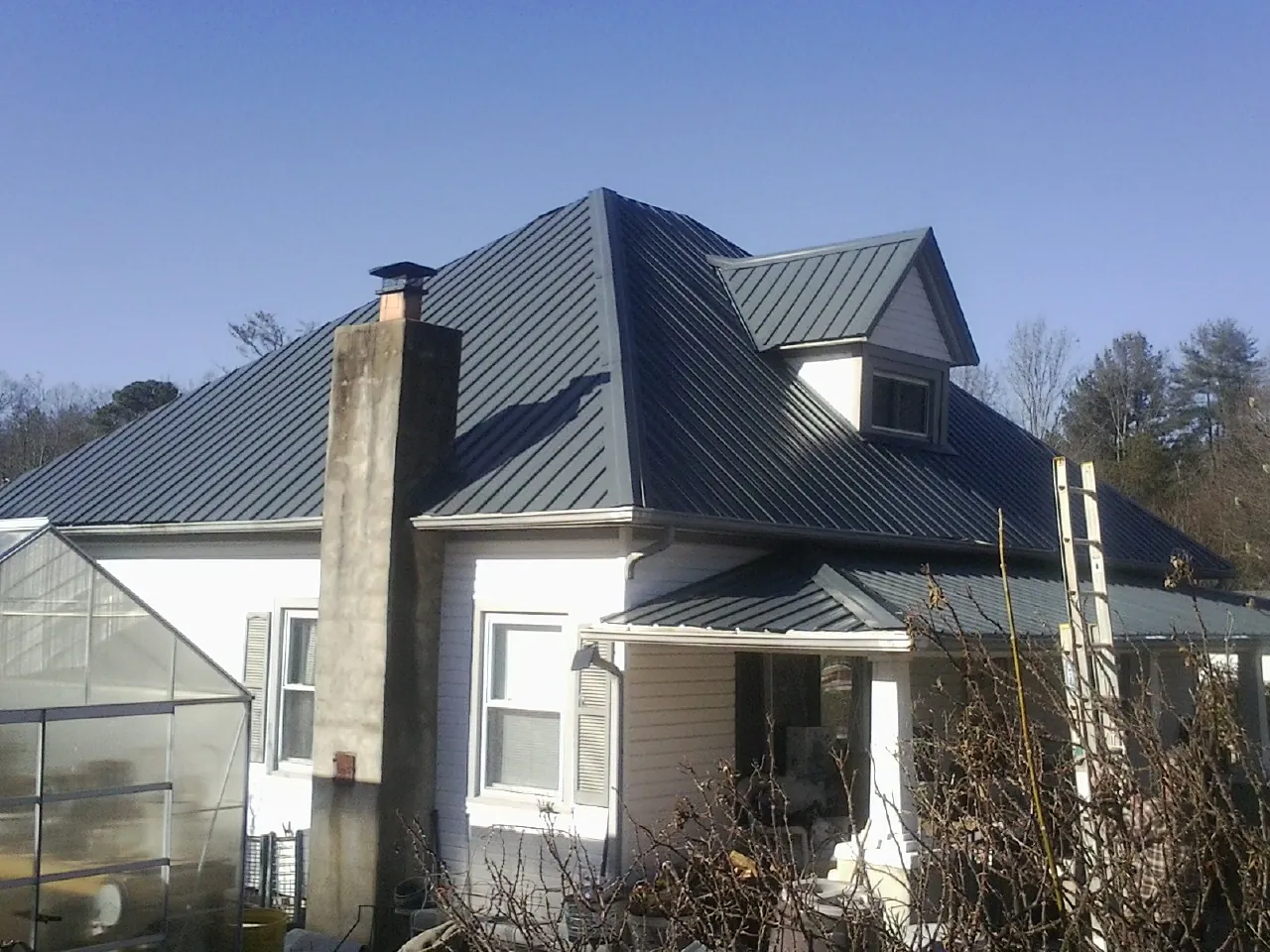 Dark blue standing seam metal roof on a white farmhouse with dormer — Slate & Tile Roof Repair by Roofing Brothers in Fort Harrison