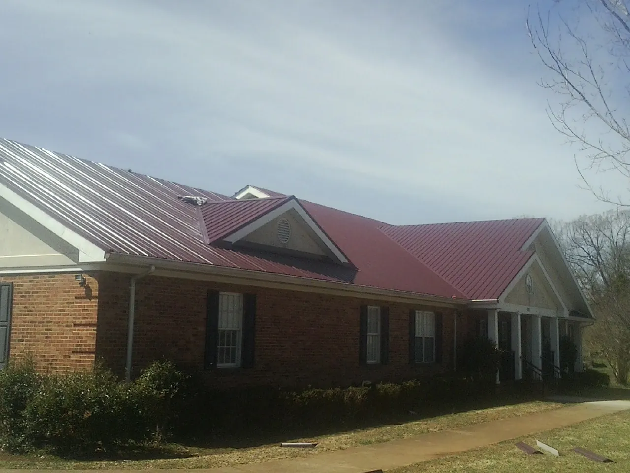 Red metal roof with gabled entries on a long brick building, from a Hail Damage Roof Repair job in Fort Harrison