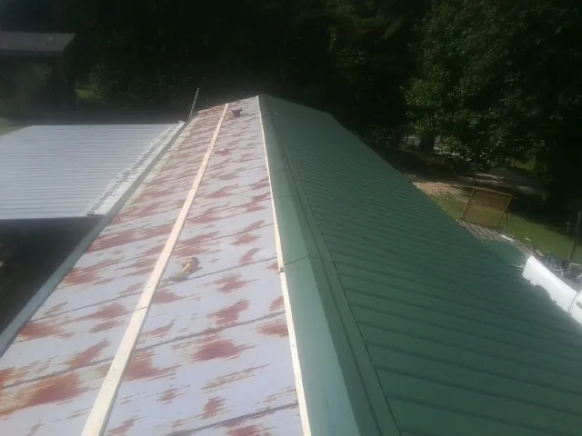 Old rusted panels beside newly installed green metal roofing — Wind Damage Roof Repair by Roofing Brothers in Fort Harrison