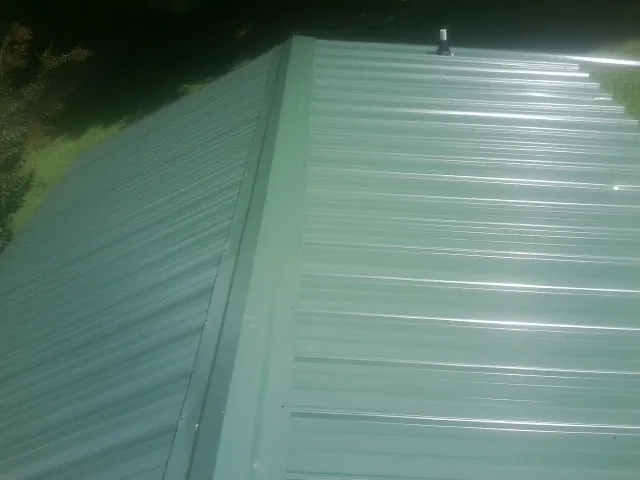 New green metal panels meeting at the ridge of a roof — Flat Roof Repair work by our crew in Fort Harrison