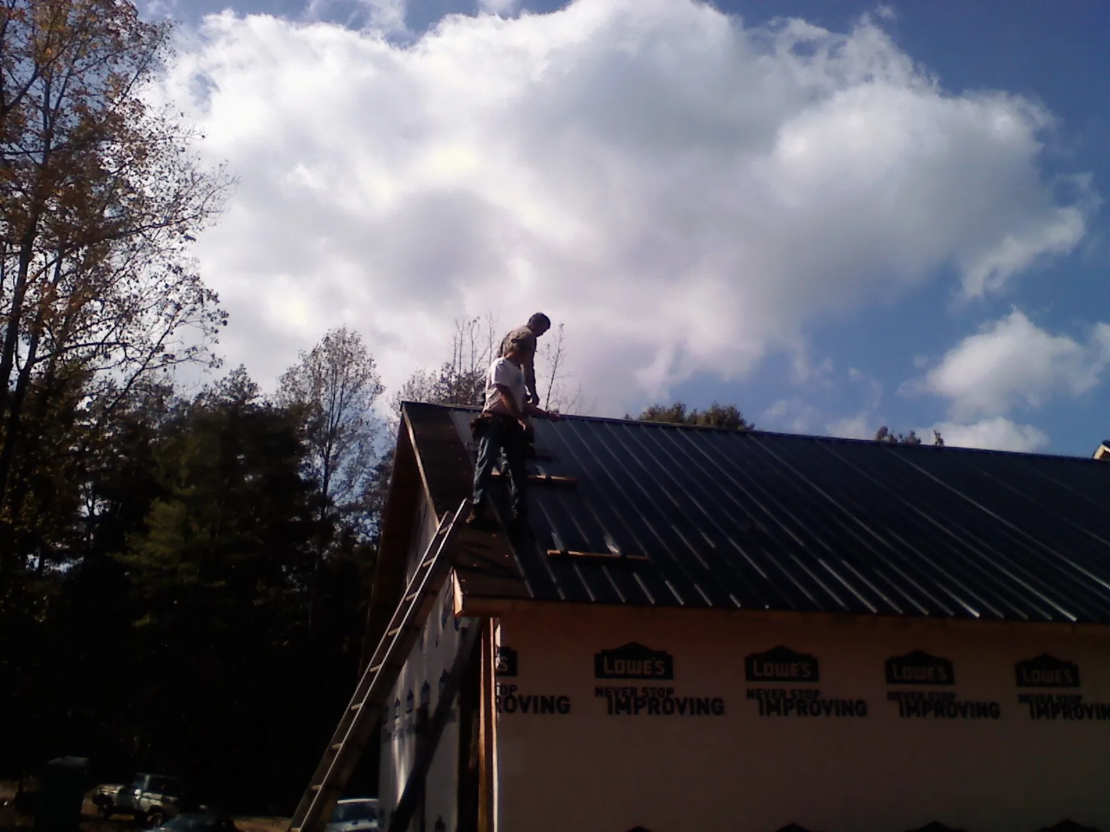 Roofer fastening dark metal panels high against a cloudy sky, from a Roof Inspection job in Fort Harrison