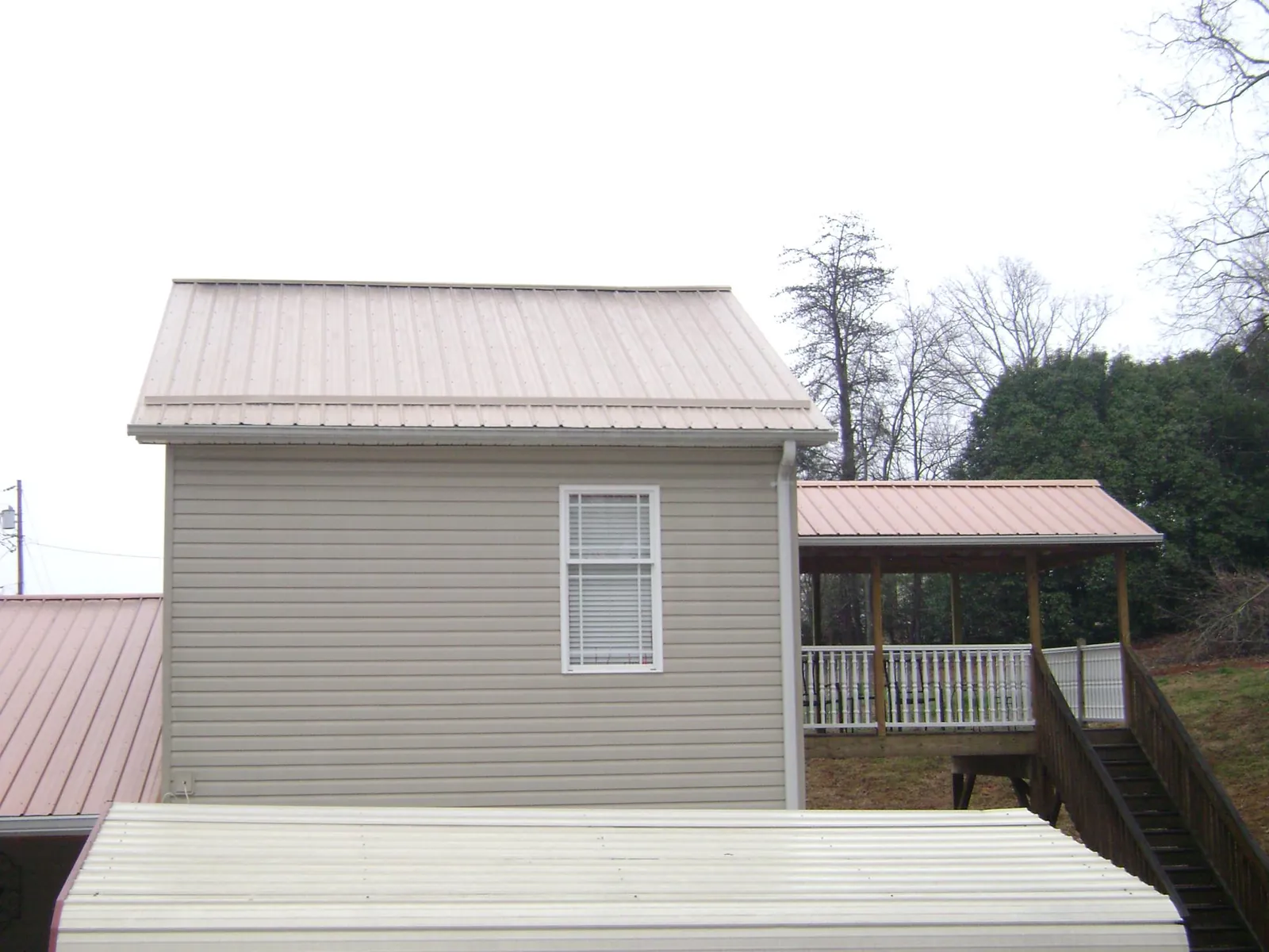 Tan metal roofs on a two story addition and attached porch, from a Roof Replacement job in Fort Harrison