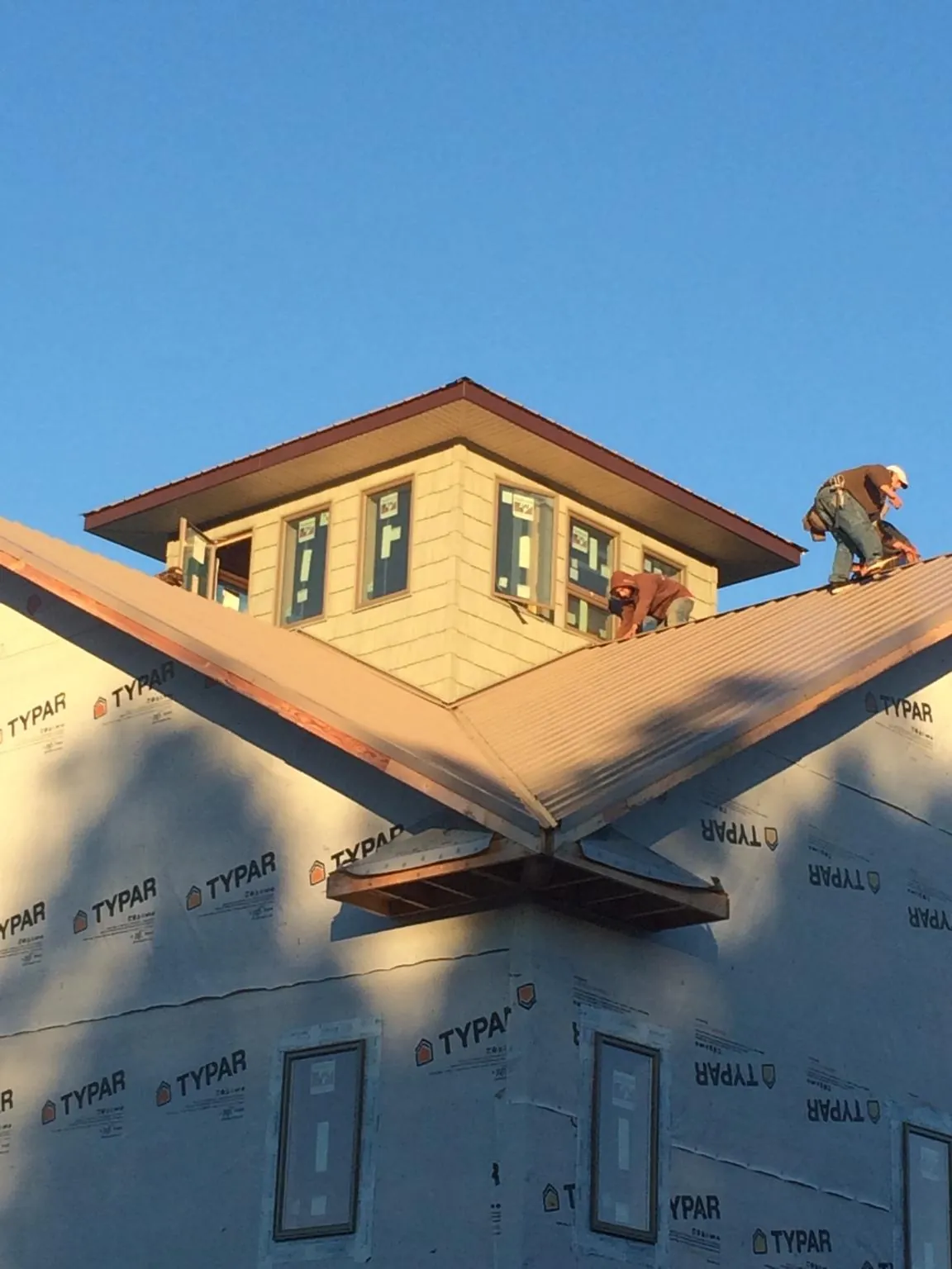 Roofers working around a rooftop cupola on a new metal roof at sunset — Roof Waterproofing in Fort Harrison by Roofing Brothers